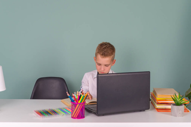 Okula dönün! Şirin, çalışkan bir çocuk okulda bir dizüstü bilgisayarın başında oturuyor. Çocuk sınıfta ders çalışıyor. - Fotoğraf, Görsel