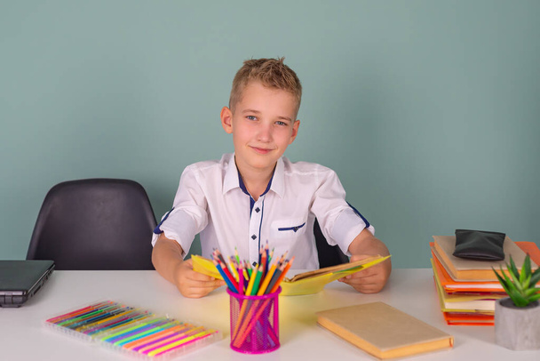 Επιστροφή στο σχολείο και ευτυχισμένη στιγμή! Ένα χαριτωμένο σκληρά εργαζόμενο παιδί κάθεται σε ένα τραπέζι στο σχολείο. αγόρι που σπουδάζει στην τάξη - Φωτογραφία, εικόνα