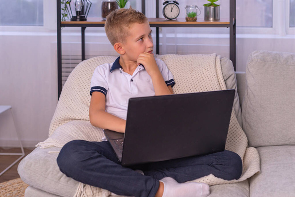 παιδί αγόρι στα ακουστικά χρησιμοποιεί ένα φορητό υπολογιστή και να μελετήσει σε απευθείας σύνδεση με το δάσκαλο βιντεοκλήσεων στο σπίτι. κατ 'οίκον διδασκαλία, εξ αποστάσεως μάθηση - Φωτογραφία, εικόνα