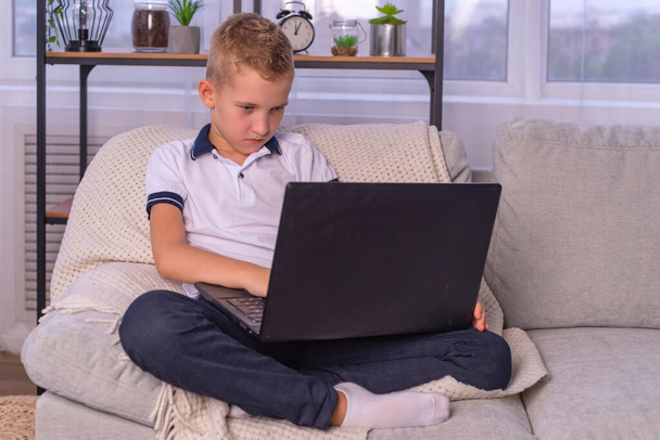 παιδί αγόρι στα ακουστικά χρησιμοποιεί ένα φορητό υπολογιστή και να μελετήσει σε απευθείας σύνδεση με το δάσκαλο βιντεοκλήσεων στο σπίτι. κατ 'οίκον διδασκαλία, εξ αποστάσεως μάθηση - Φωτογραφία, εικόνα