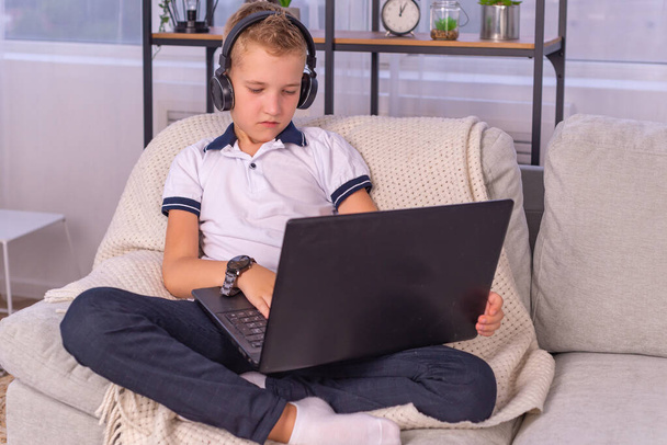 chłopiec w słuchawkach jest za pomocą laptopa i uczyć się online z nauczycielem rozmowy wideo w domu. edukacja domowa, kształcenie na odległość - Zdjęcie, obraz