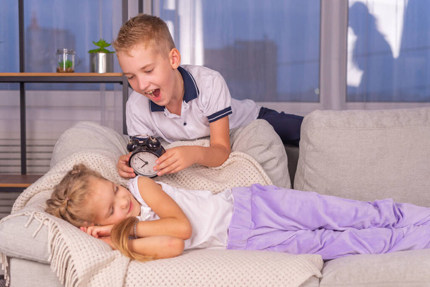 ein Mädchen und ein Junge Schulkinder mit einem Wecker, der laut ruft, wollen morgens nicht aufwachen - Foto, Bild