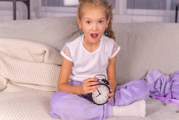 schoolgirl girl with an alarm clock who calls loudly does not want to wake up in the morning - Foto, Imagem