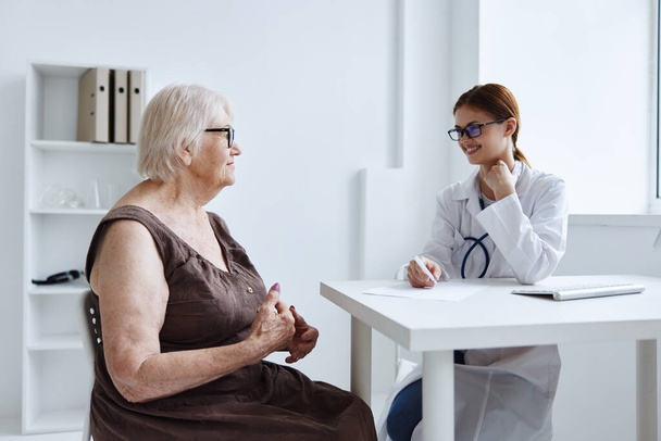ηλικιωμένη γυναίκα με γυαλιά που μιλάει στο ιατρικό γραφείο της νοσοκόμας - Φωτογραφία, εικόνα