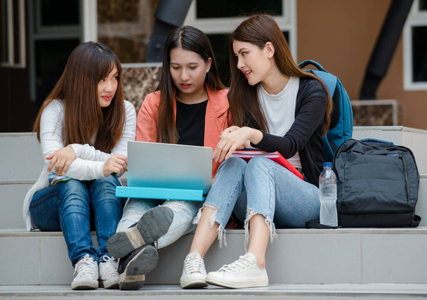Gruppe von drei jungen attraktiven asiatischen Studentinnen, die zusammen mit Laptop auf dem Campus der Universität im Freien sitzen und studieren. Konzept für Bildung, Freundschaft und Studentenleben. - Foto, Bild