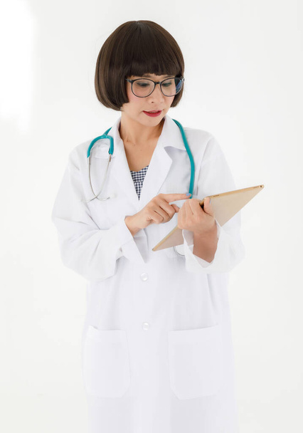 Professional young Asian female medic in white coat and glasses with stethoscope on neck checking data on digital tablet while working in clinic - Zdjęcie, obraz