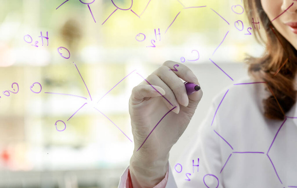 Colheita cientista feminina irreconhecível com marcador escrevendo fórmulas químicas em placa de vidro enquanto trabalhava com colegas em laboratório. - Foto, Imagem