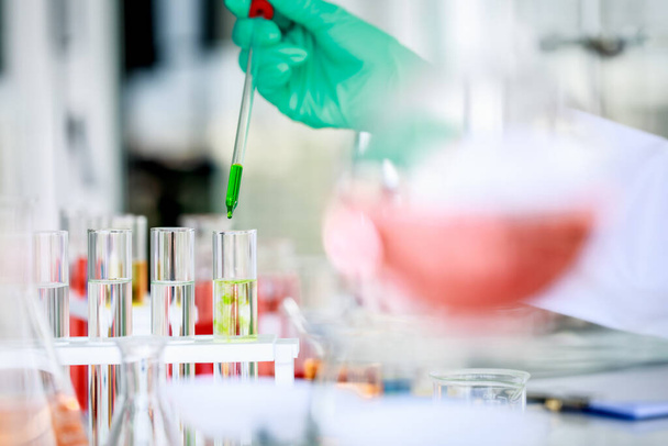 Anonieme wetenschapper in pipet gieten van groene vloeistof in glazen reageerbuis tijdens het uitvoeren van chemisch onderzoek in het laboratorium. - Foto, afbeelding