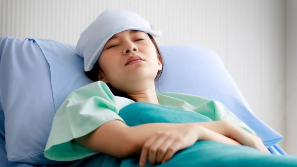 Azjatka młoda piękna pacjentka choruje, leży i śpi w łóżku w szpitalu z fajnym opakowaniem na czole, aby złagodzić gorączkę. Koncepcja leczenia i zdrowia - Zdjęcie, obraz