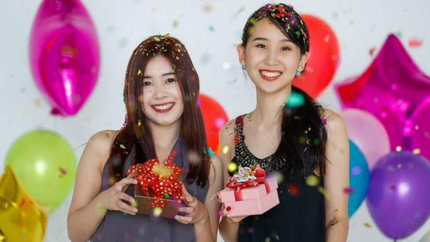 Optimista fiatal aranyos ázsiai nők ajándékdobozokkal áll a színes konfetti alatt, kamerába néz és mosolyog az ünnepek alatt. Jó idő megosztása és fesztivál ünneplik koncepció. - Fotó, kép