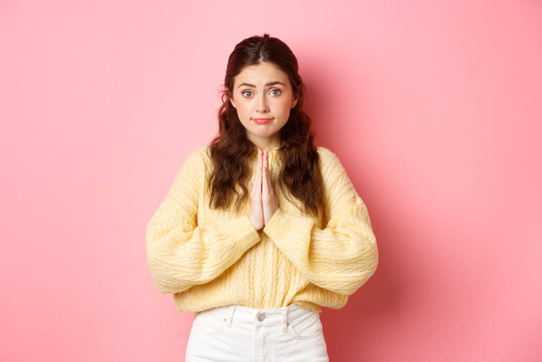 Please. Cute lady asking for favour, begging you, holding hands in pleading gesture and gazing at camera, standing over pink background - Photo, Image