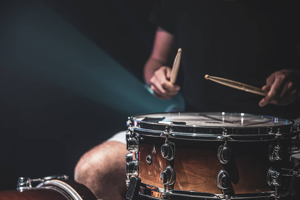 Primer plano de un baterista tocando un tambor con palos sobre un fondo oscuro. - Foto, imagen