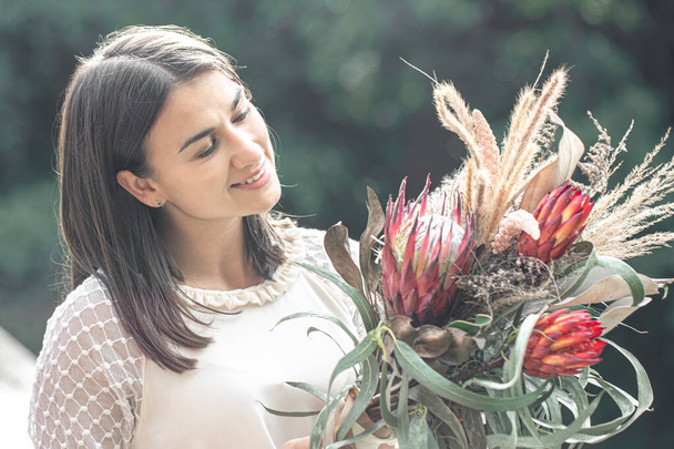 Portrait of an attractive young woman with a bouquet of exotic flowers, a bouquet with protea flowers. - Photo, Image