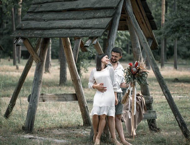 Young man and woman smartly dressed hugging in the forest with a bouquet of exotic flowers, romance in marriage. - Fotoğraf, Görsel