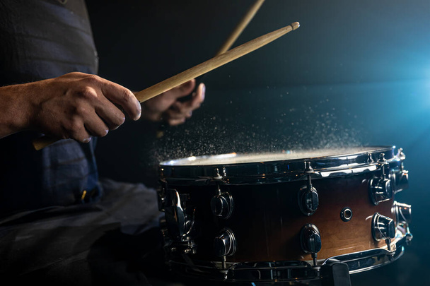 Batterista utilizzando bacchette di tamburo colpire rullante tamburo con spruzzi d'acqua su sfondo nero sotto illuminazione studio da vicino. - Foto, immagini