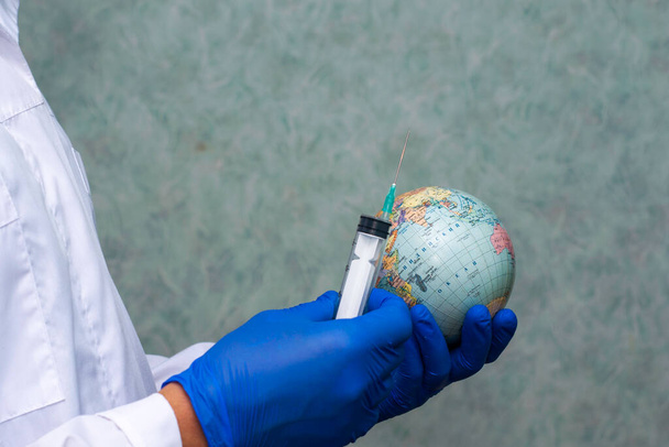 een arts in een witte jas en beschermende handschoenen houdt een injectiespuit m globus concept vaccinatie immunisatie. Hoge kwaliteit foto - Foto, afbeelding