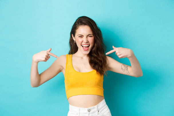 Sassy young woman yelling self-assured, pointing at herself, self-promoting, bragging about personal achievement, standing over blue background - Photo, Image