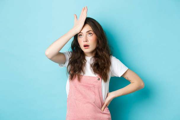 Annoyed and tired young woman in summer outfit, slap forehead and roll eyes, standing over blue background - Foto, Imagen