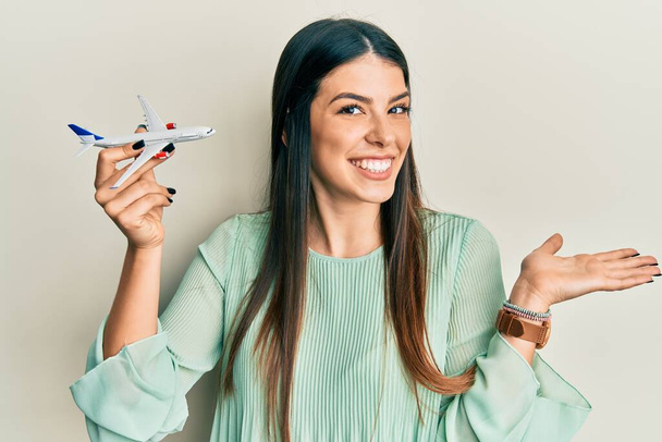 Joven mujer hispana sosteniendo juguete de avión celebrando logro con sonrisa feliz y expresión ganadora con la mano levantada  - Foto, Imagen