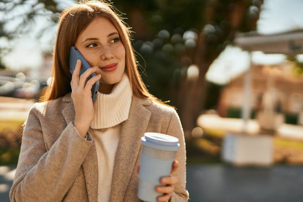 Junges rothaariges Mädchen spricht auf dem Smartphone und trinkt Kaffee in der Stadt. - Foto, Bild