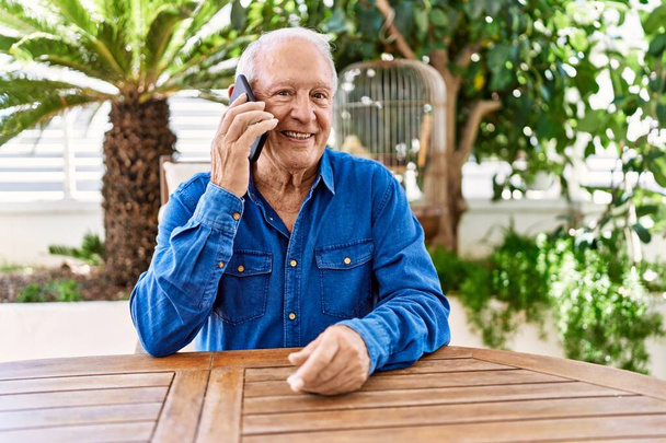 Senior kaukasischen Mann lächelt glücklich reden auf dem Smartphone sitzt auf dem Tisch auf der Terrasse. - Foto, Bild