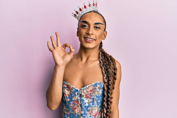 Hispanic man wearing make up and long hair wearing princess crown doing ok sign with fingers, smiling friendly gesturing excellent symbol  - Photo, Image