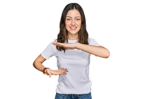 大小のサインを示す手でジェスチャーカジュアルな白いTシャツを身に着けている若い美しい女性は、シンボルを測定します。カメラを見て笑ってる。概念を測定し.  - 写真・画像