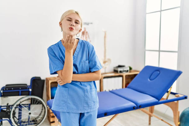 Beautiful caucasian physiotherapist woman working at pain recovery clinic looking at the camera blowing a kiss with hand on air being lovely and sexy. love expression.  - Photo, Image