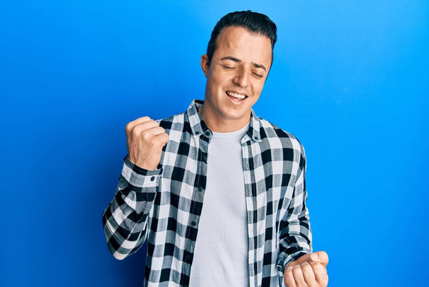 Όμορφος νεαρός άνδρας φορώντας casual πουκάμισο γιορτάζει έκπληκτος και έκπληκτος για την επιτυχία με τα χέρια ψηλά και τα μάτια κλειστά  - Φωτογραφία, εικόνα