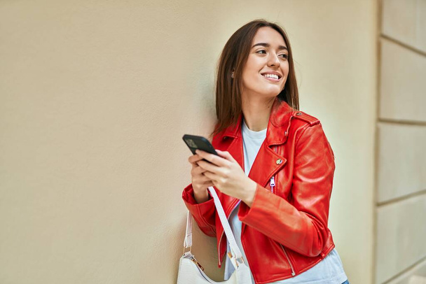 Young hispanic woman smiling happy using smartphone at the city. - Photo, Image