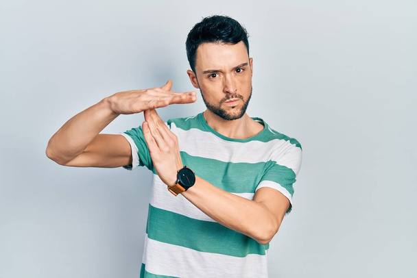 Fiatal spanyol férfi visel alkalmi ruhák csinál idő out gesztus kezével, frusztrált és komoly arc  - Fotó, kép