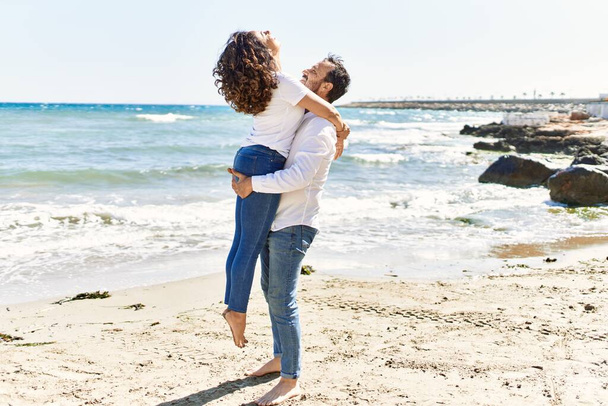Latynoska para w średnim wieku uśmiecha się szczęśliwa i przytula na plaży. - Zdjęcie, obraz
