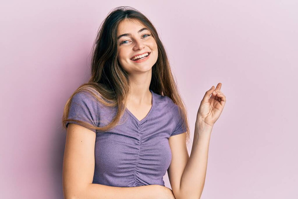 Young caucasian woman wearing casual clothes with a big smile on face, pointing with hand and finger to the side looking at the camera.  - Zdjęcie, obraz