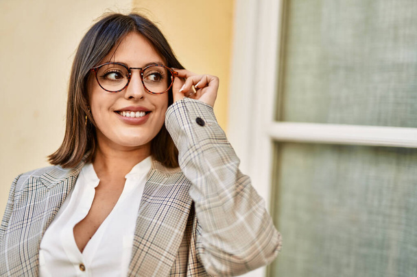 Νεαρή Ισπανίδα επιχειρηματίας χαμογελά ευτυχισμένη κρατώντας γυαλιά στην πόλη. - Φωτογραφία, εικόνα