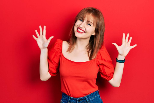 roodharige jonge vrouw draagt casual rood t shirt tonen en wijzen met vingers nummer tien terwijl glimlachen zelfverzekerd en gelukkig.  - Foto, afbeelding