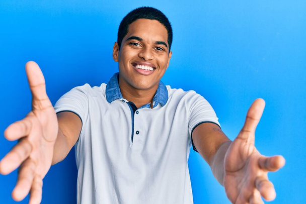 Young handsome hispanic man wearing casual clothes looking at the camera smiling with open arms for hug. cheerful expression embracing happiness.  - Foto, Imagen