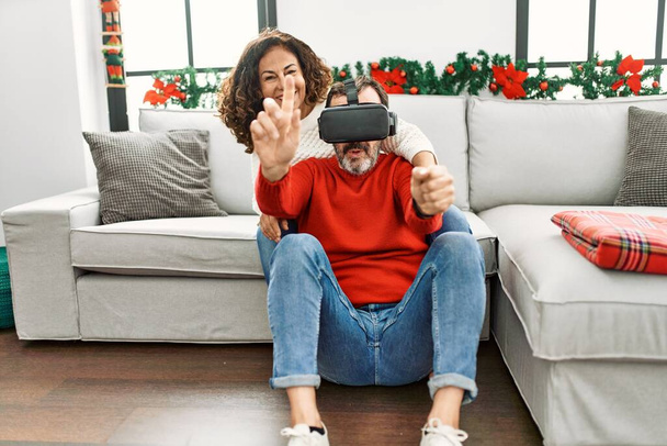 Middle age hispanic couple smiling happy sitting on the sofa playing with virtual reality glasses at home. - Foto, Imagem