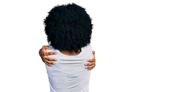 Młoda Afroamerykanka, ubrana w luźną białą koszulę, przytulająca się od tyłu i szczęśliwa. miłość własna i opieka własna  - Zdjęcie, obraz