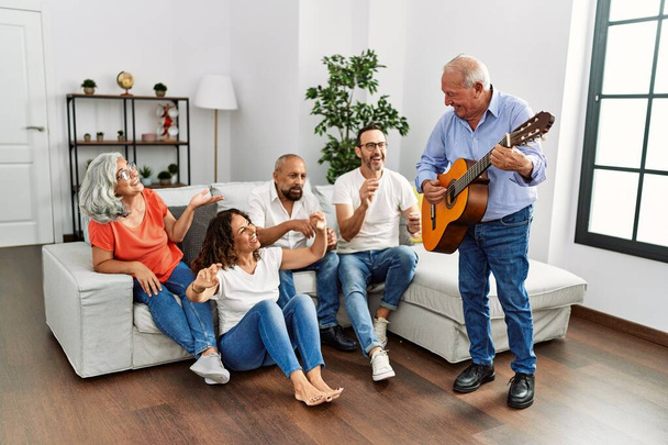 Grupa przyjaciół w średnim wieku o partii gra na gitarze klasycznej siedzi na kanapie w domu. - Zdjęcie, obraz