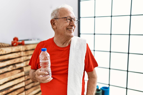 Starszy mężczyzna w odzieży sportowej i ręczniku na siłowni odwraca wzrok z uśmiechem na twarzy, naturalnym wyrazem twarzy. śmiać się pewnie.  - Zdjęcie, obraz