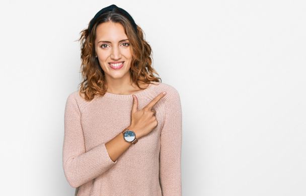 Beautiful young caucasian woman wearing casual sweater cheerful with a smile on face pointing with hand and finger up to the side with happy and natural expression  - Photo, Image