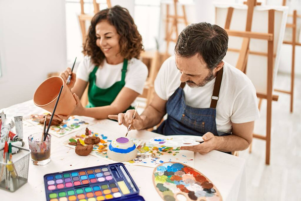 Δύο μαθητές μέσης ηλικίας χαμογελώντας ευτυχισμένη ζωγραφική γλυπτική πηλό στη σχολή καλών τεχνών. - Φωτογραφία, εικόνα