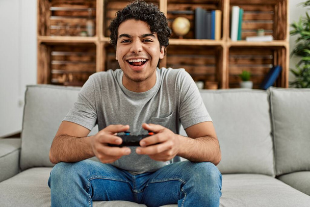 Young hispanic man playing video game sitting on the sofa at home. - Photo, image