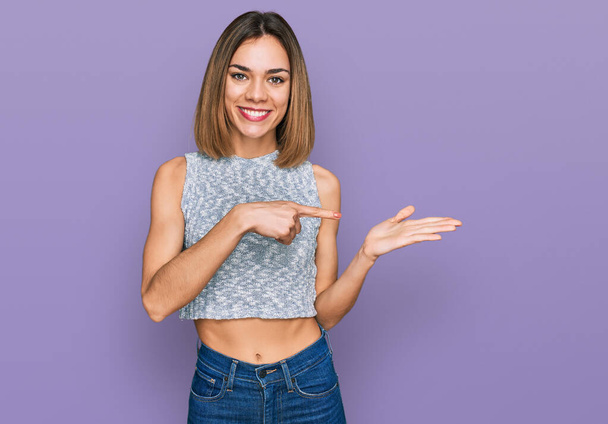 Young blonde girl wearing casual style with sleeveless shirt amazed and smiling to the camera while presenting with hand and pointing with finger.  - Фото, изображение