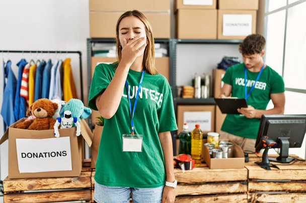 Young blonde girl wearing volunteer t shirt at donation stand bored yawning tired covering mouth with hand. restless and sleepiness.  - Photo, Image