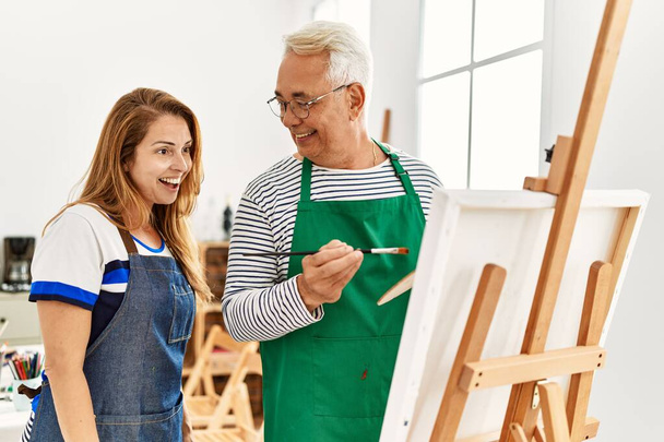 Middelbare leeftijd verf leraar en student glimlachen gelukkig schilderen in kunststudio. - Foto, afbeelding