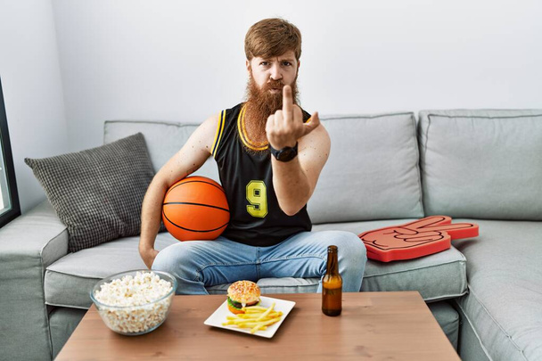 Caucasian man with long beard holding basketball ball cheering tv game showing middle finger, impolite and rude fuck off expression  - Photo, image