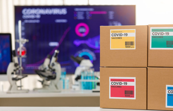 Selektywny nacisk na opakowanie szczepionek Covid 19 w pudełka z wyodrębnionymi kolorami, siedzące w laboratorium z rozmytymi mikroskopami i tubą medyczną w tle. Koncepcja szczepienia szczepionką Covid 19. - Zdjęcie, obraz
