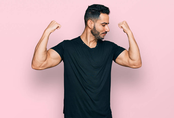 Hispanic man with beard wearing casual black t shirt showing arms muscles smiling proud. fitness concept.  - Photo, Image
