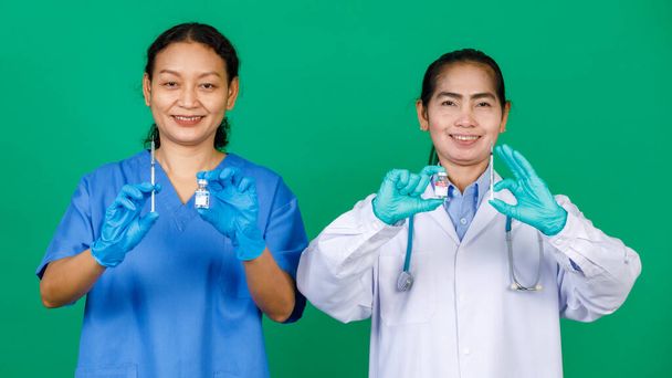 Азиатская медсестра в халате и доктор в белом халате, держащая шприц и вакцину Ковид 19, готовящуюся к инъекции. Концепция вакцинации против ковида 19. - Фото, изображение